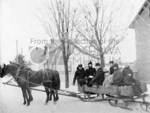 Black and white photo of a sleigh full of people being pulled by two horses