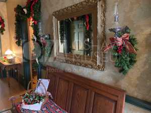 Colour photo of a hallway with a wooden bench and a mirror above it. It is decorated with holiday greenery and ribbons