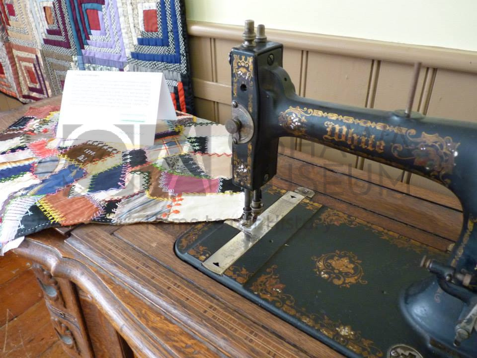 A vintage, black metal sewing machine with a colourful quilt square on the sewing machine's work surface
