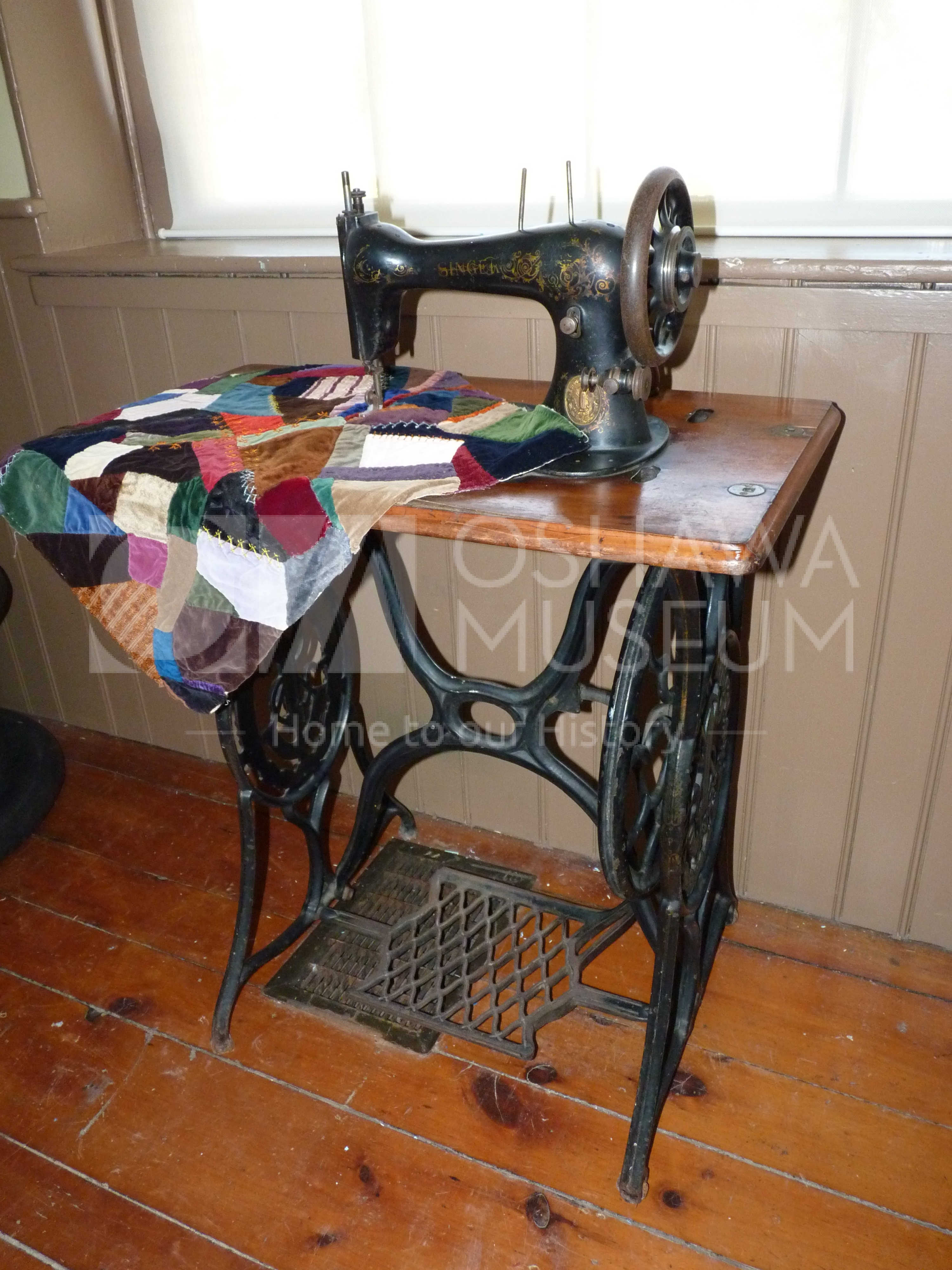A wood and metal sewing machine with a colourful quilt square on the work surface of the sewing machine